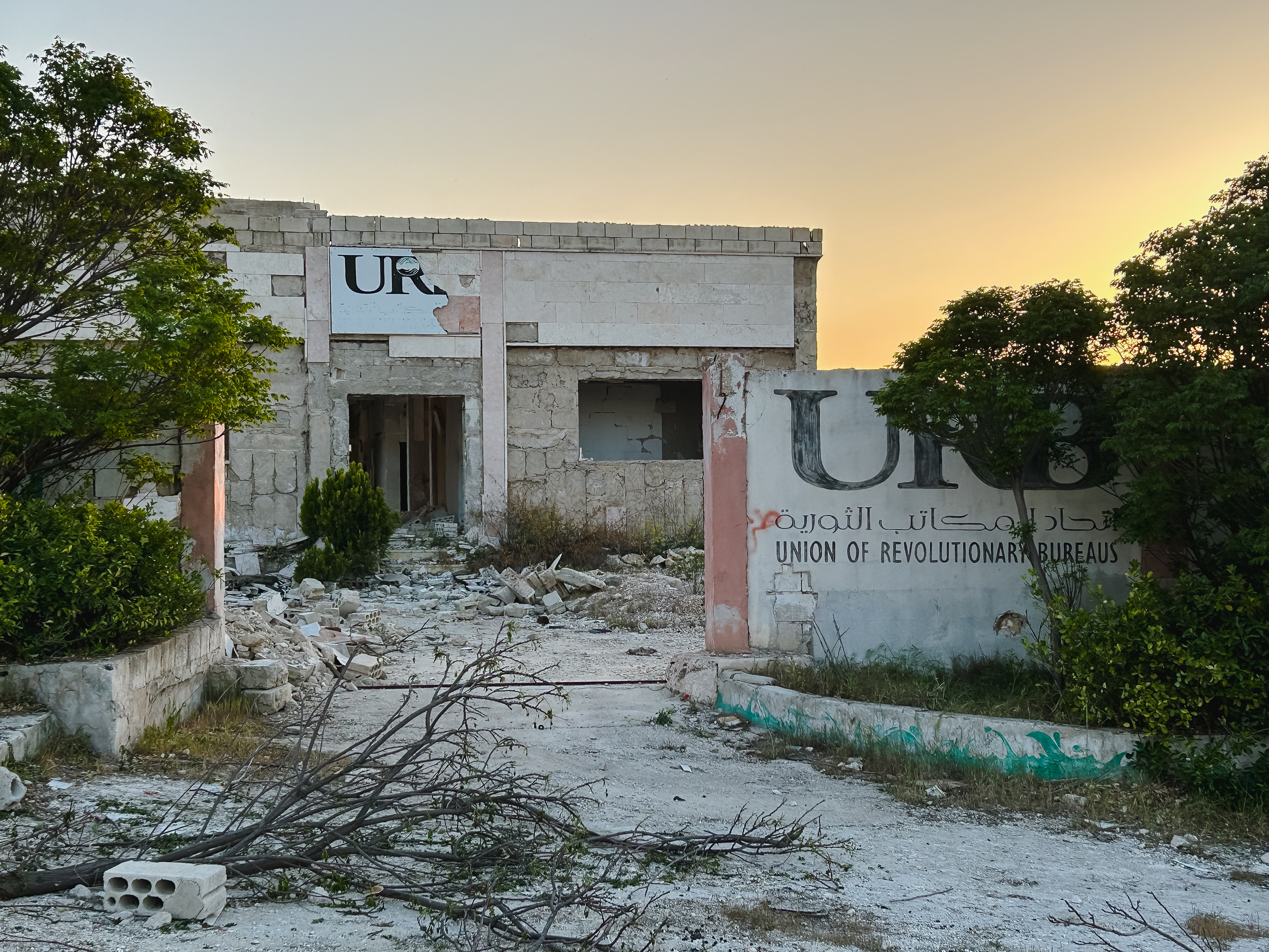 كفرنبل في أبريل/نيسان 2025. (Photo: Qantara/Kristin Helberg) يمكن رؤية مبنى مدمر وجدار بجانبه مكتوب عليه "اتحاد مكاتب الثورة".
