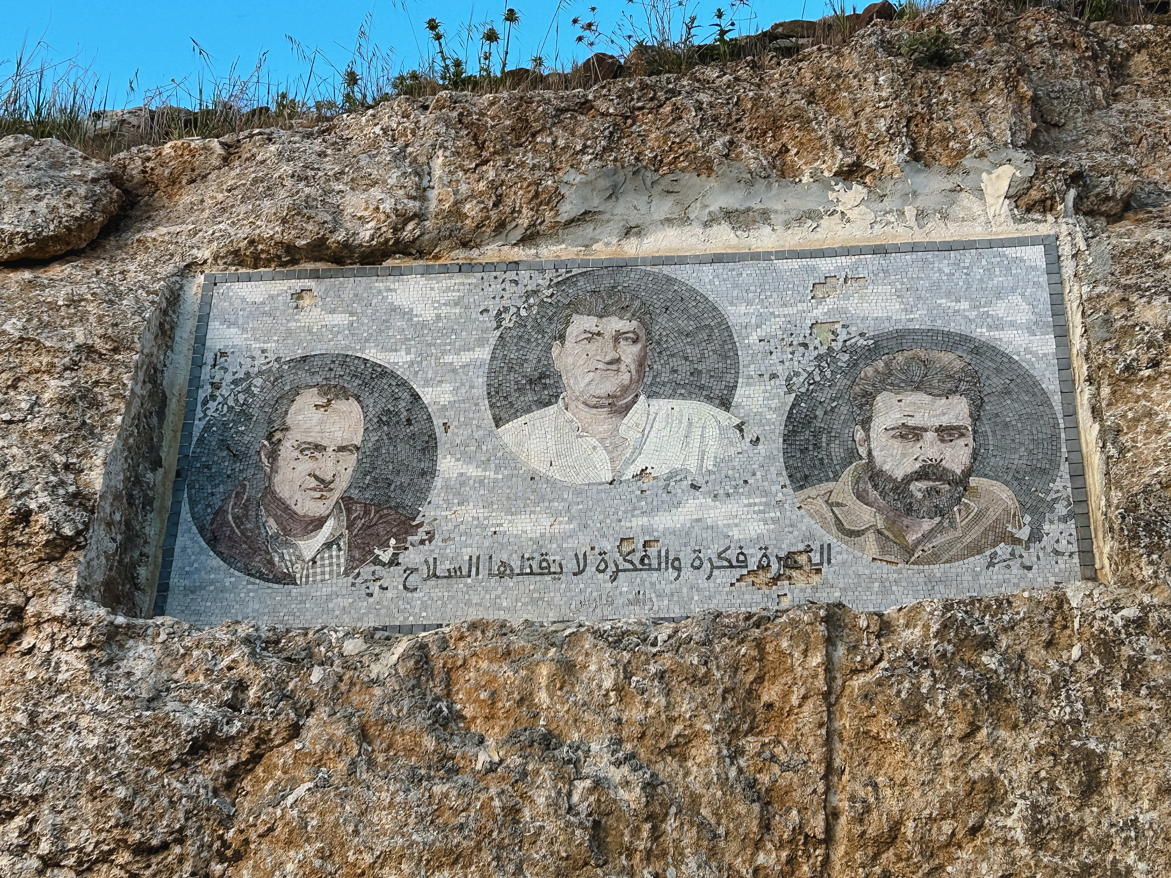 An der Wand ist ein Mosaik mit drei Männern zu sehen, und darunter steht auf Arabisch: „Revolution ist eine Idee, und eine Idee kann nicht mit Waffen getötet werden.“ (Foto: Qantara/Kristin Helberg) An der Wand ist ein Mosaik mit drei Männern zu sehen, und darunter steht auf Arabisch: „Revolution ist eine Idee, und eine Idee kann nicht mit Waffen getötet werden.“