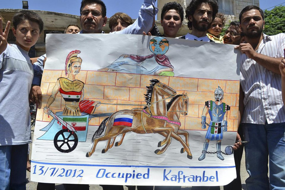 Kafranbell July 2012. (Photo: Qantara/ ZDF/ Markus Hertrich Demonstranten in Kafranbel tragen ein Schild mit der englischen Aufschrift „Kafranbell Occupied”.