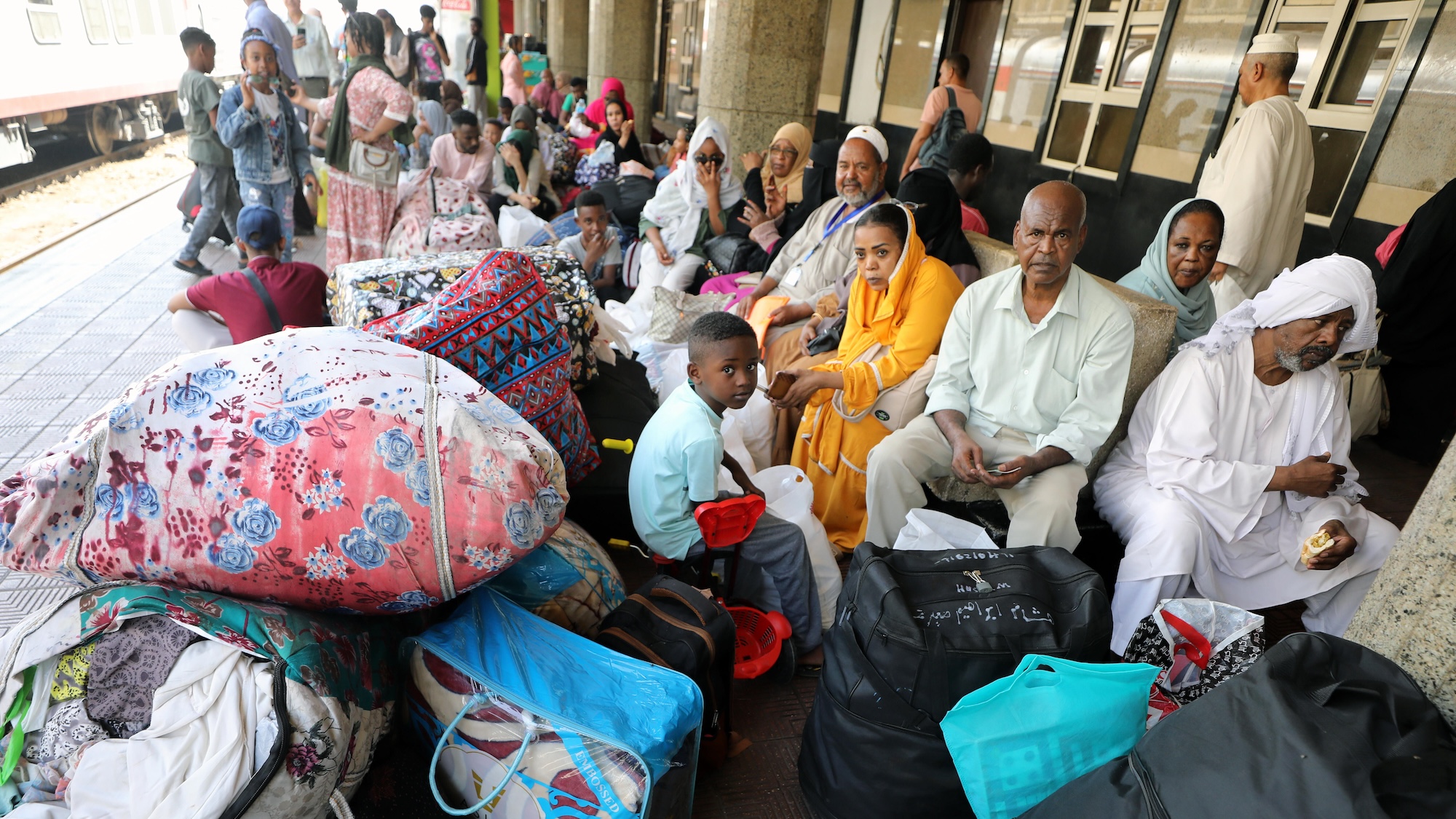 A group of people sit on a train platform surrounded by luggage.