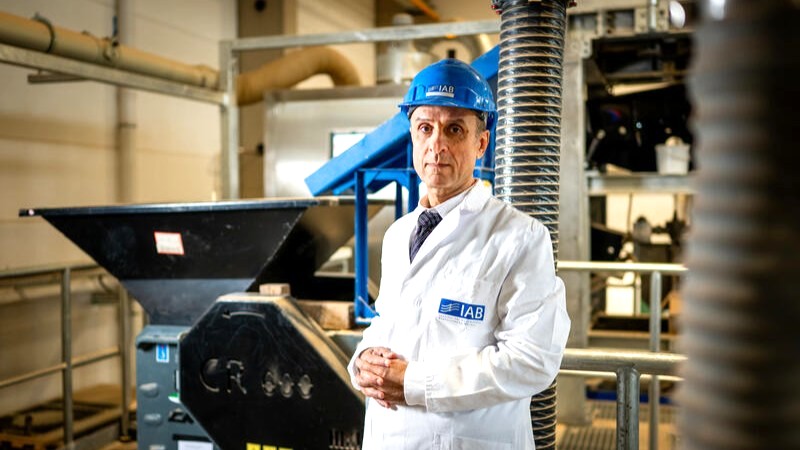 Aref al-Swaidani. Foto: Institut für Angewandte Bauforschung Weimar Ein Mann mit blauem Schutzhelm und weißem Kittel steht in einer Werkhalle.