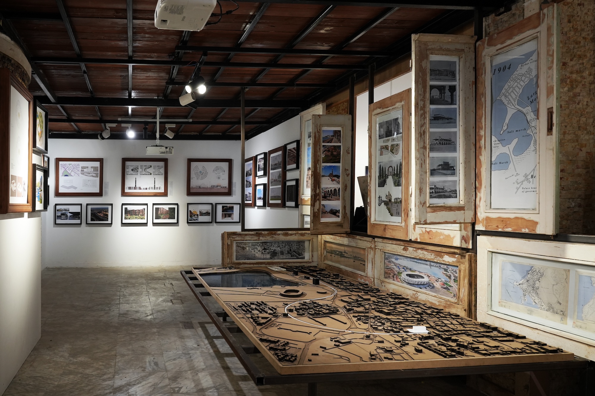 A hallway with pictures hanging on the walls and an architectural model mounted on a table in the centre.