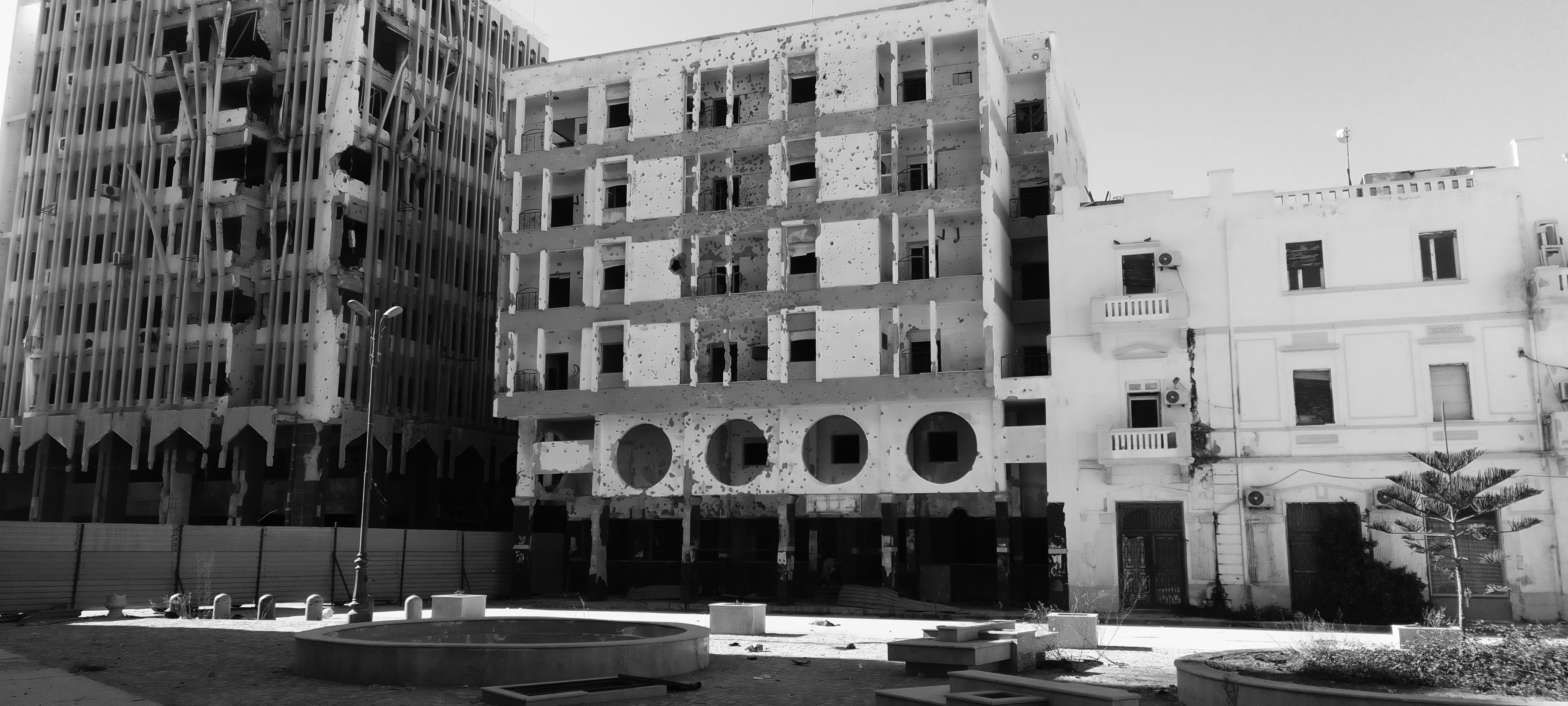 Black and white photo of three buildings, two are very damaged and one on the right has been restored.