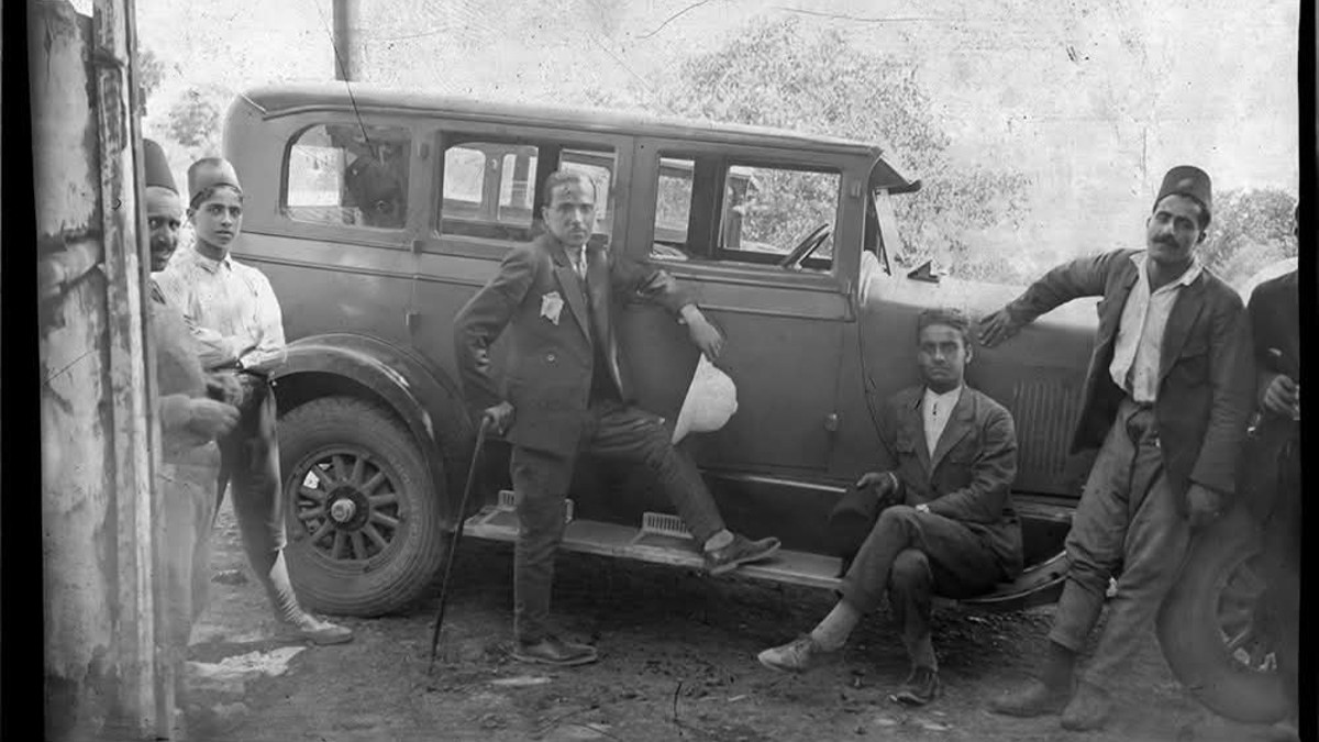 Schwarz-weiß-Bild: Eine Gruppe Männer posieren vor einem Auto.