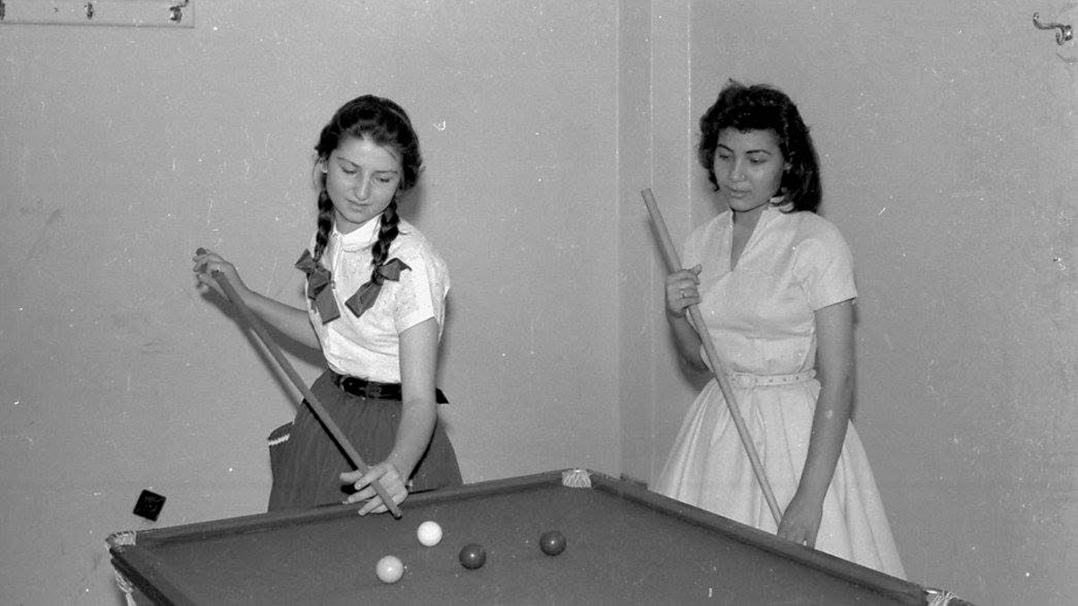 Schwarz-weiß Bild: zwei junge Frauen spielen Billiard.