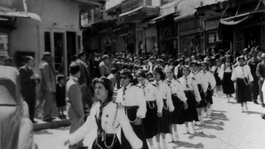 Schwarz-weiß Bild: Eine Gruppe junger Frauen in Uniform marschiert durch eine Straße.