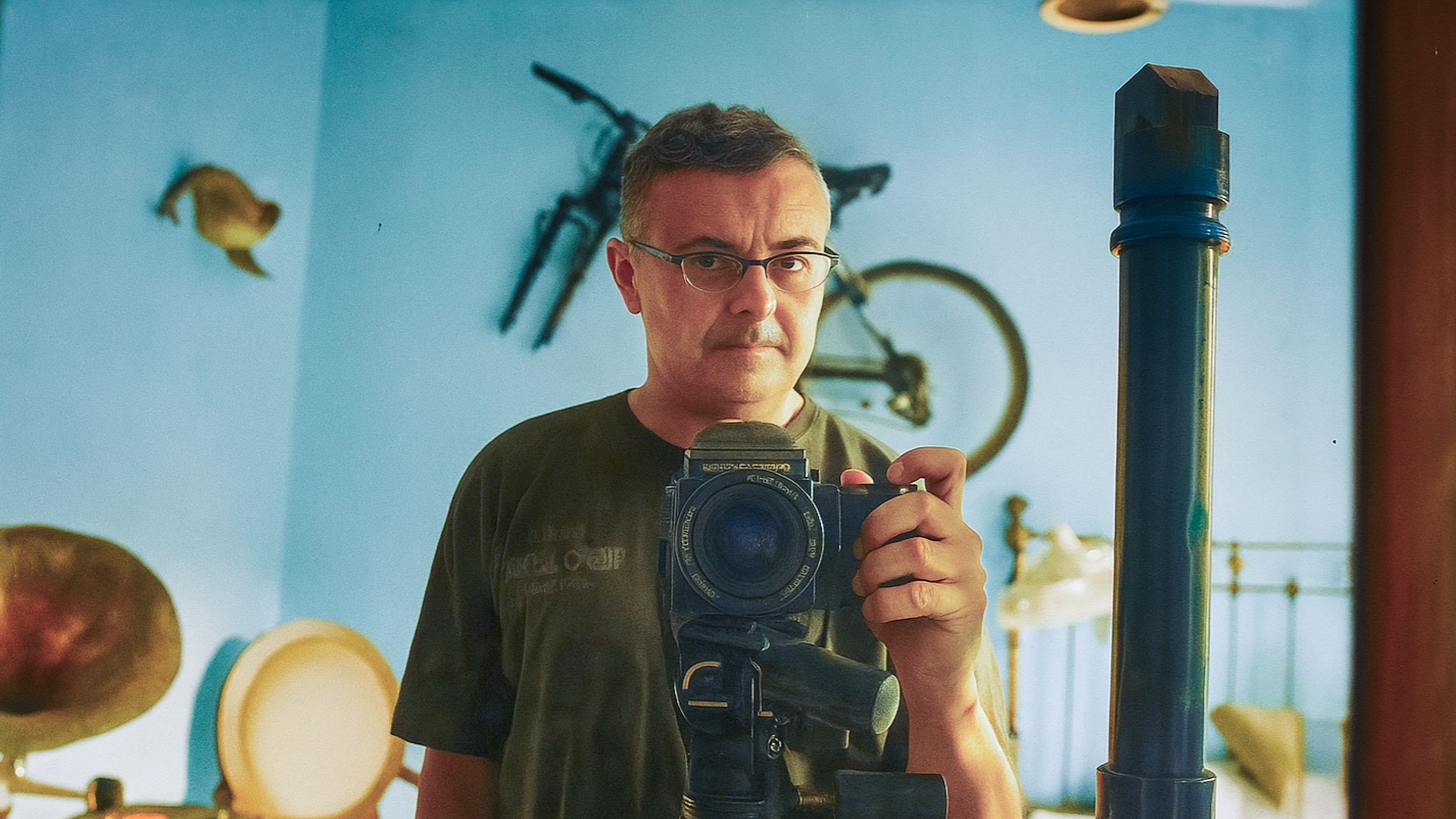 Ein Mann mit Brille steht hinter seiner Kamera und macht ein Foto im Spiegell.