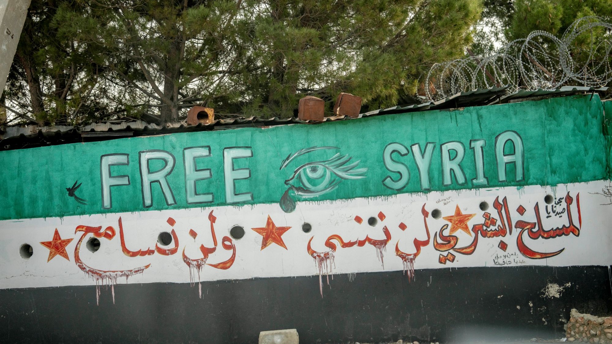 Eine Mauer ist mit der neuen syrischen Flagge bemalt. Darauf steht "Free Syria" und auf Arabisch: "Sednaja-Gefängnis, das menschliche Schlachthaus: Kein Vergeben, kein Vergessen."