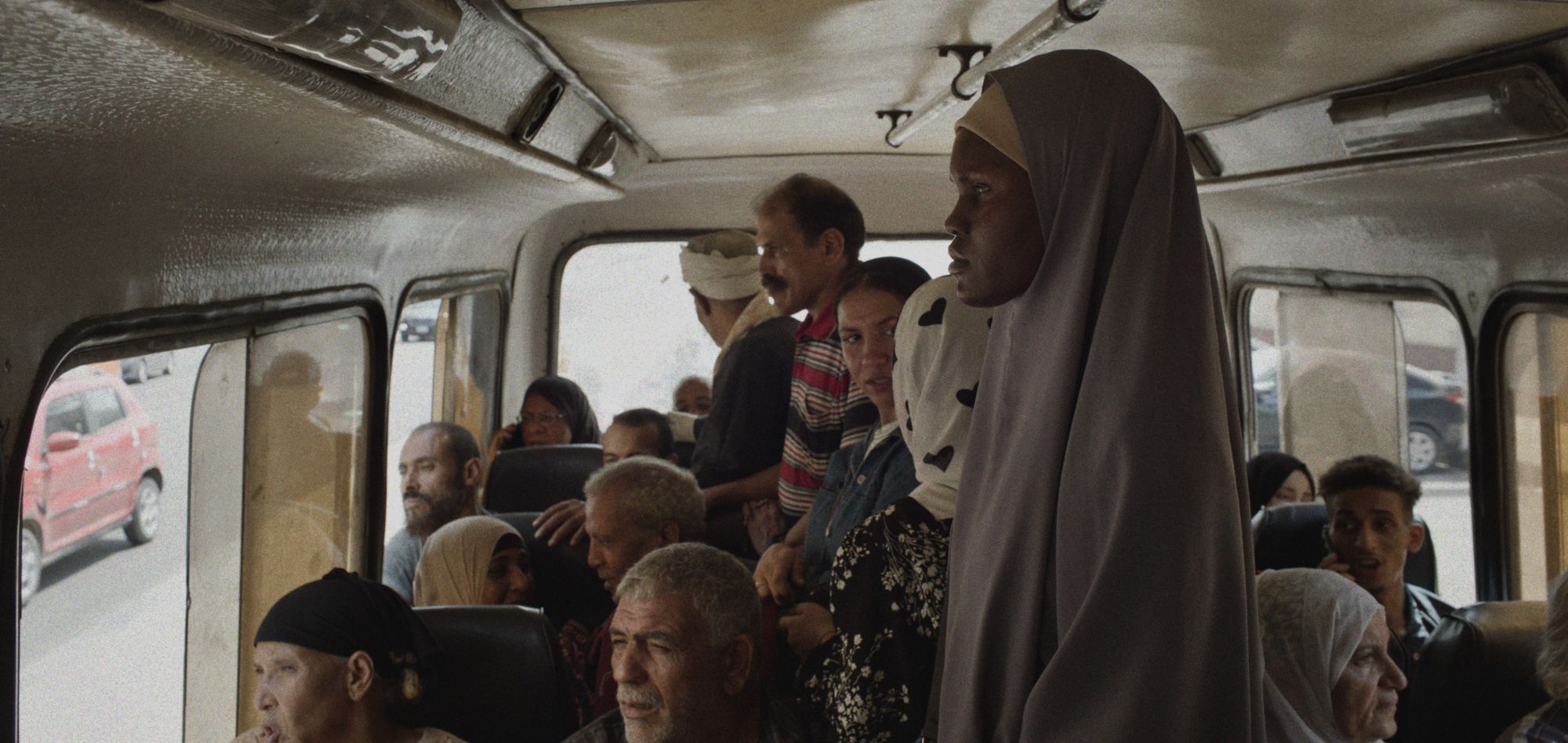 The main character is standing in a public minibus, surrounded by other passengers.