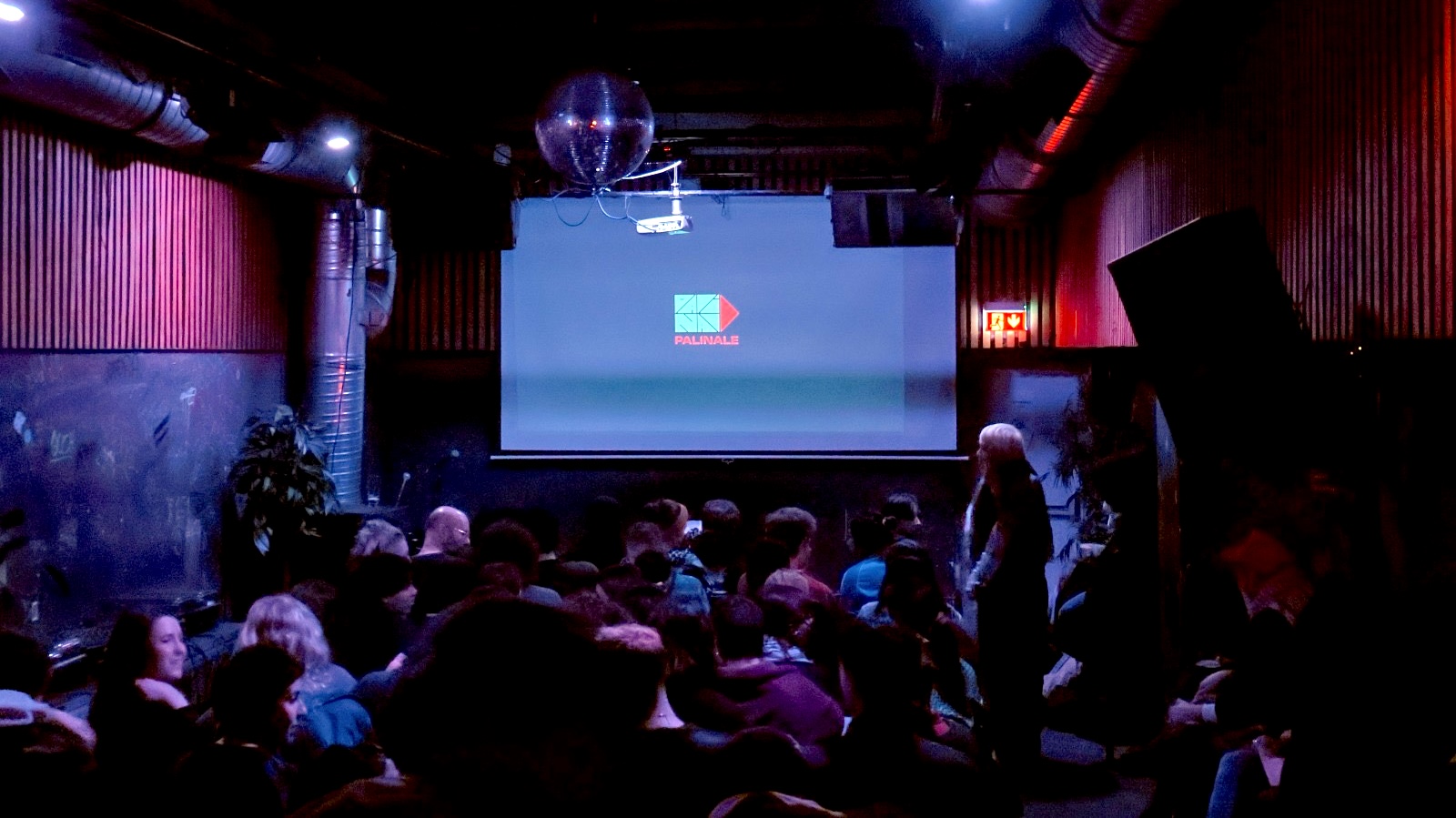 A crowded room full of people. On a screen at the front, the words "Palinale" and a logo.