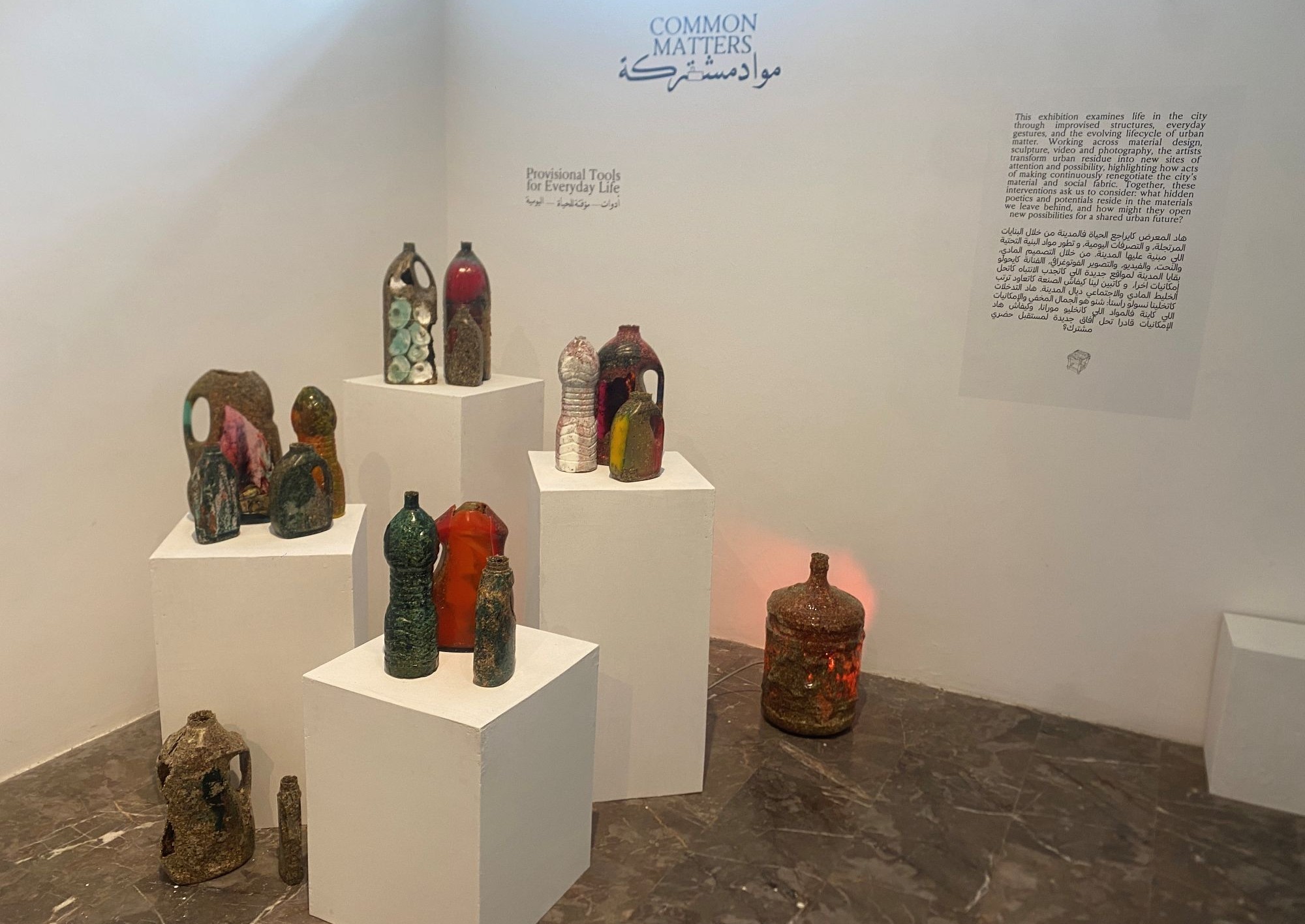 A selection of bottles and other objects around a room. On the wall is text with the title "Common Matters"