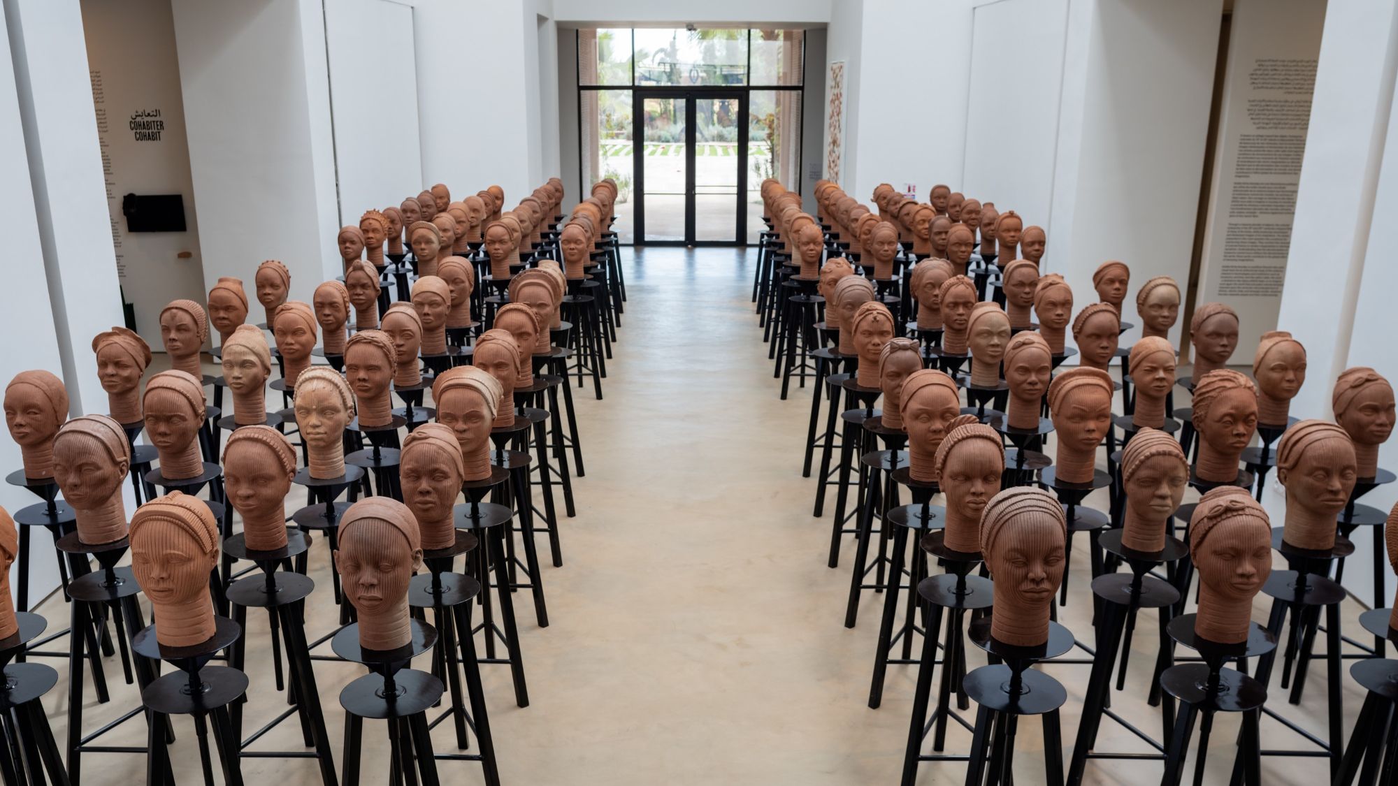 Clay sculptures of heads are arranged in rows in a gallery.