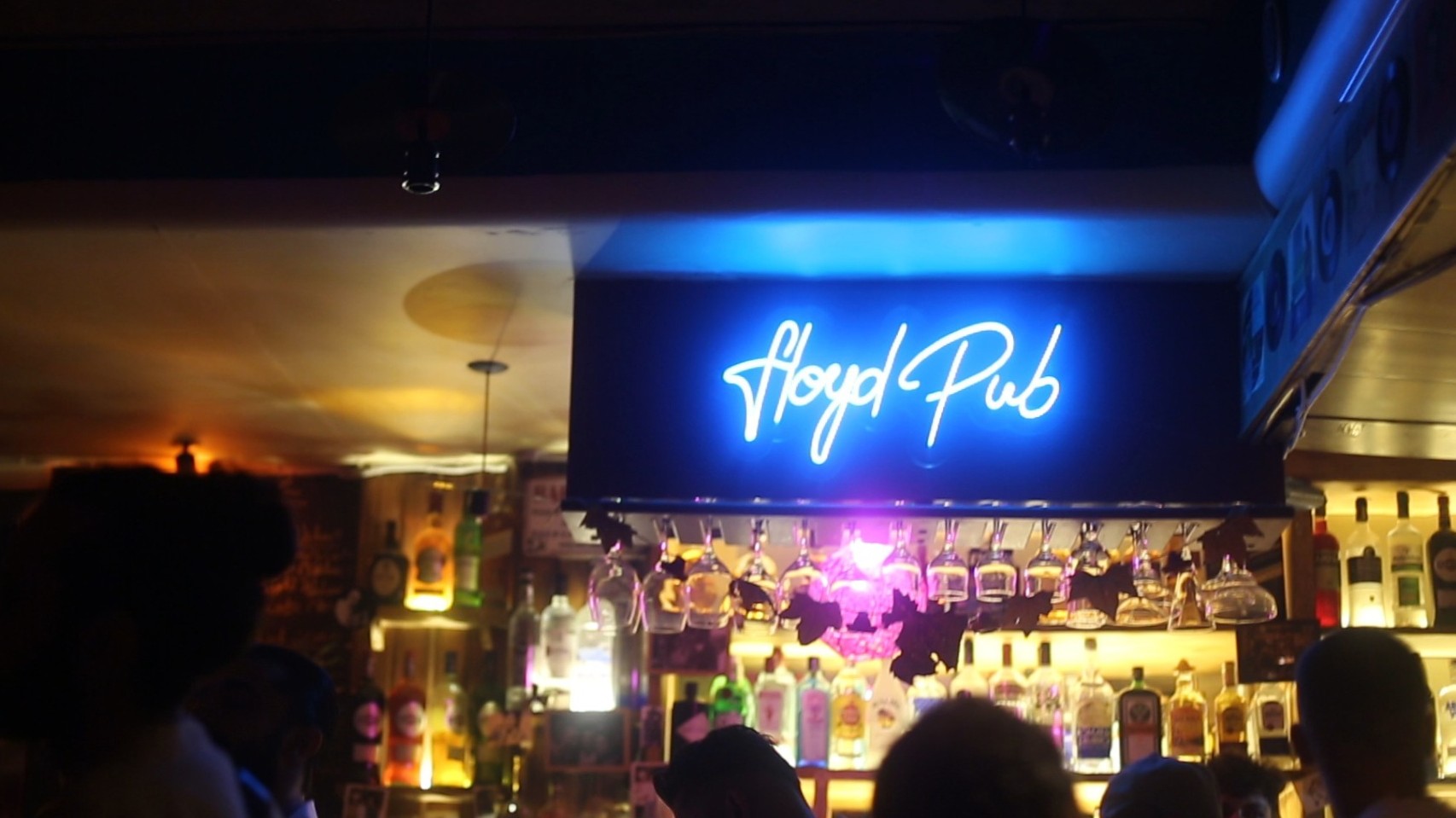 Innenraum einer Bar mit Leuchtreklame über den Köpfen der Gäste, dort steht "Floyd"
