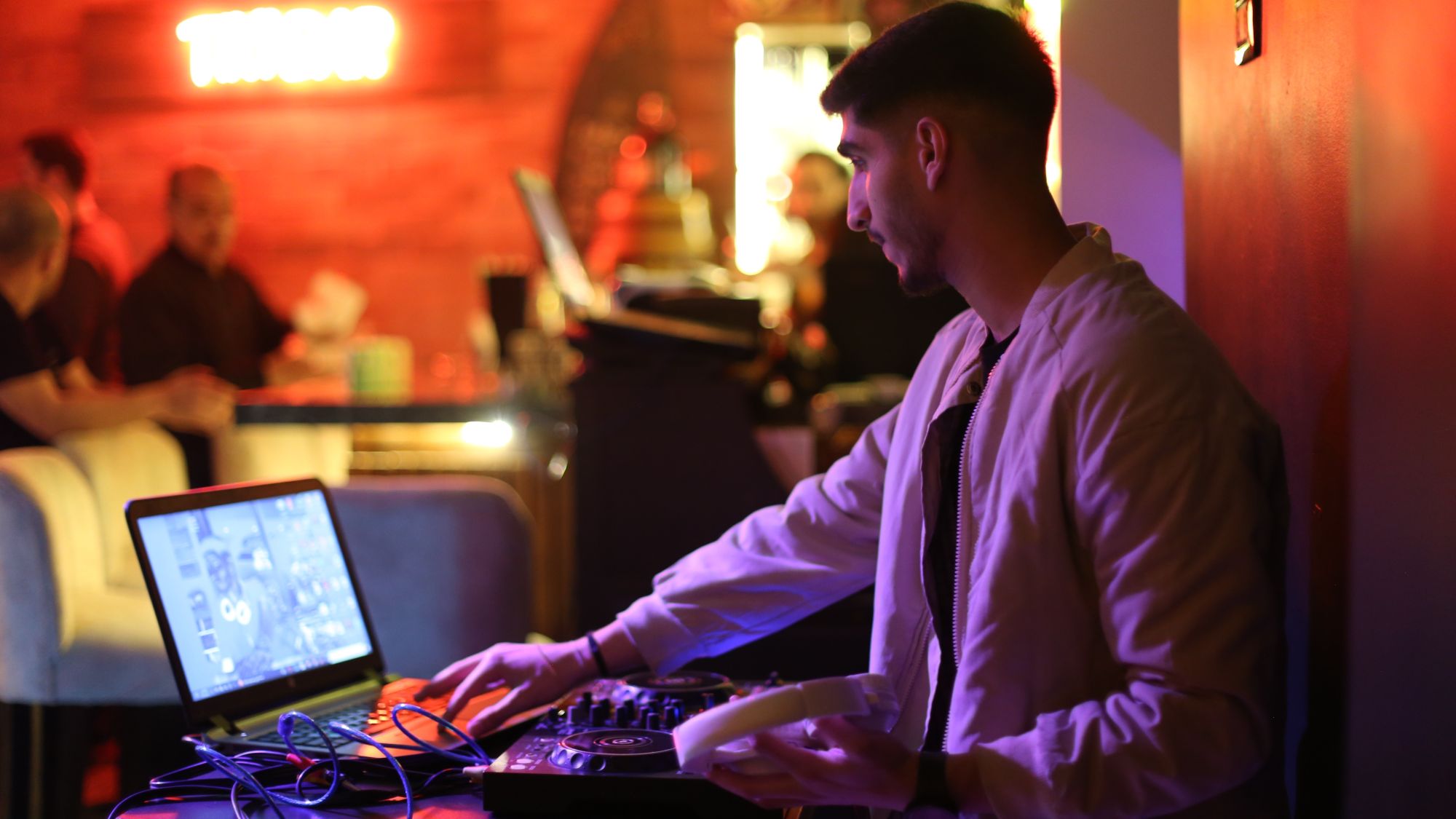 Ein DJ am Pult, im Hintergrund Gäste.