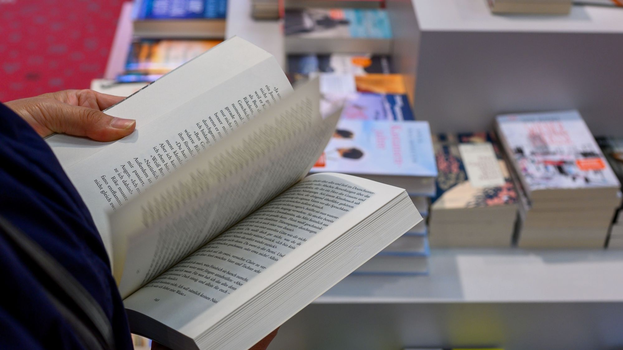 Hände, die ein Buch aufschlagen. Im Hintergrund verschwommen eine Bücherauslage.