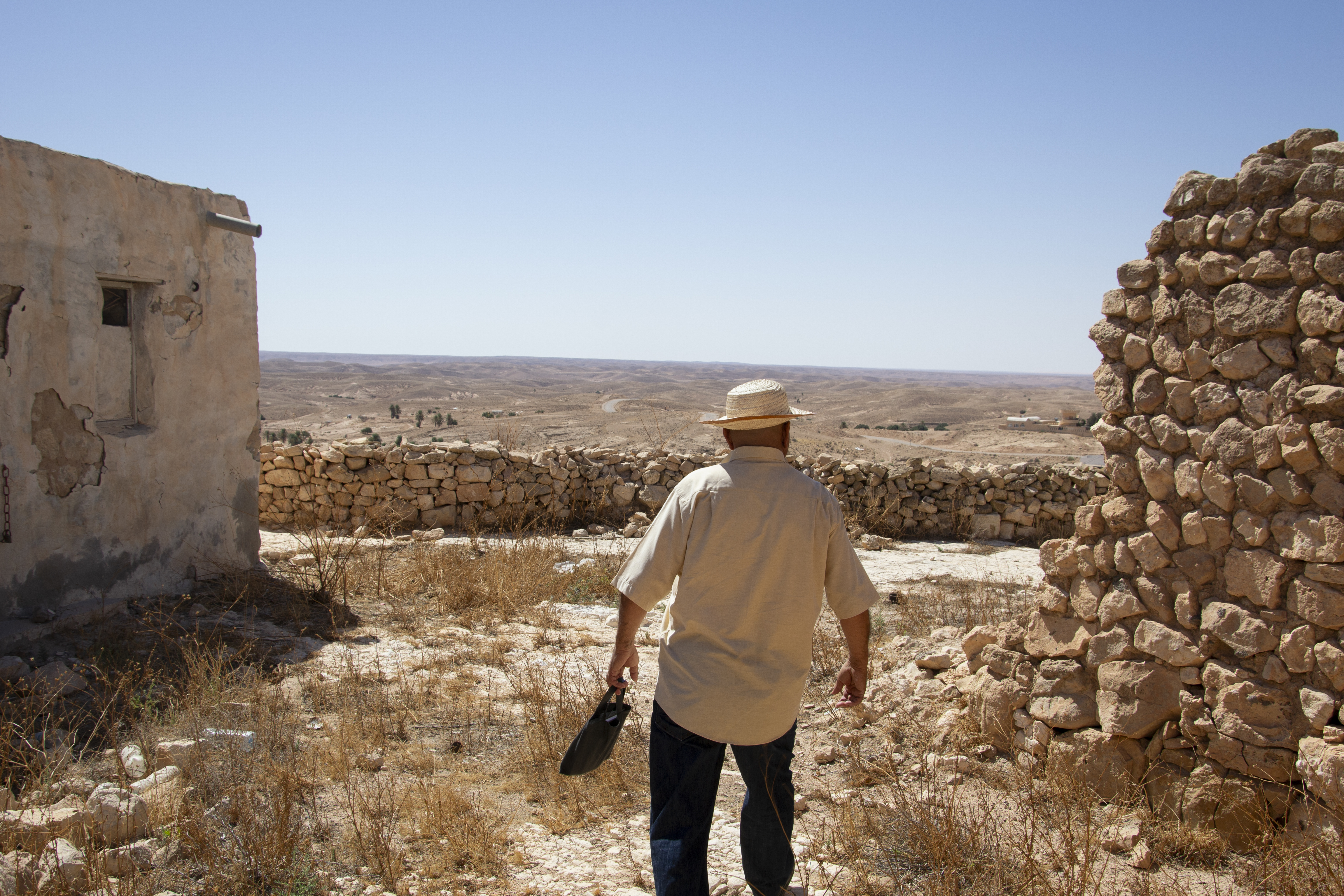 A man walks away from the camera. In front of him is a view across a vast landscape.