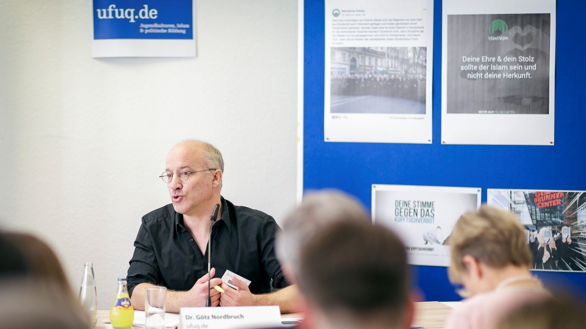 Ein Mann spricht zu einem Publikum, hinter ihm Materialien des Vereins ufuq.de