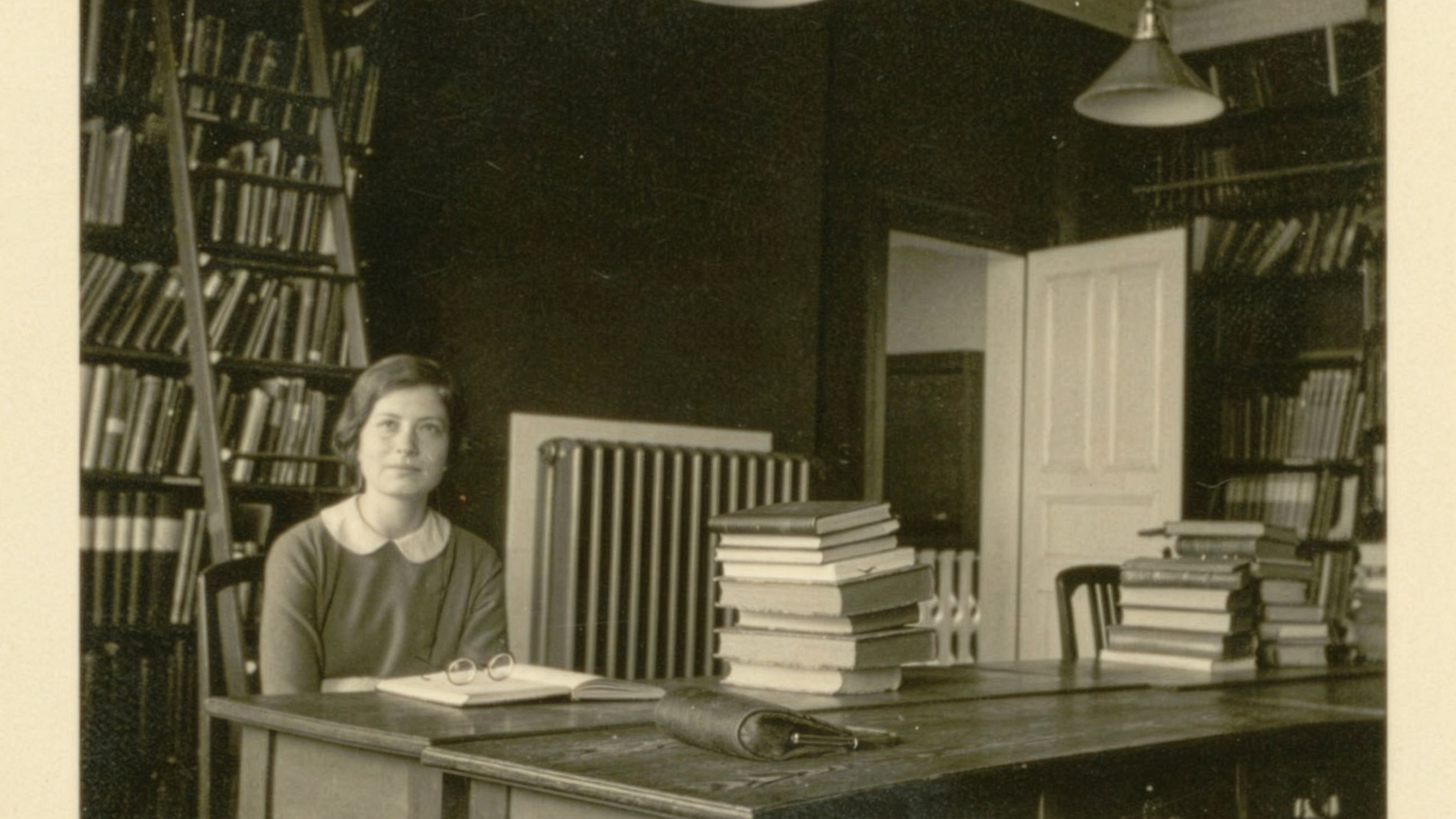 A black and white image of a young woman sitting in a room full of books.