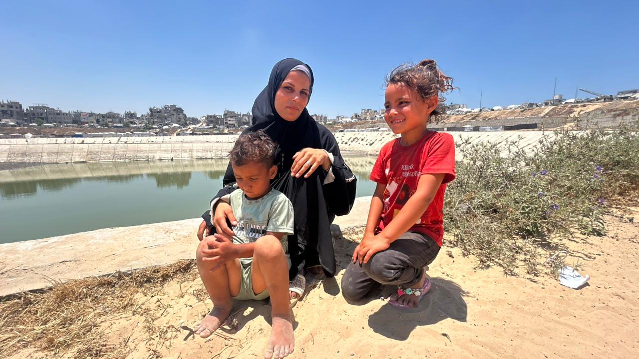 امرأة شابة وبجوارها طفلين على حافة بركة مياه.
