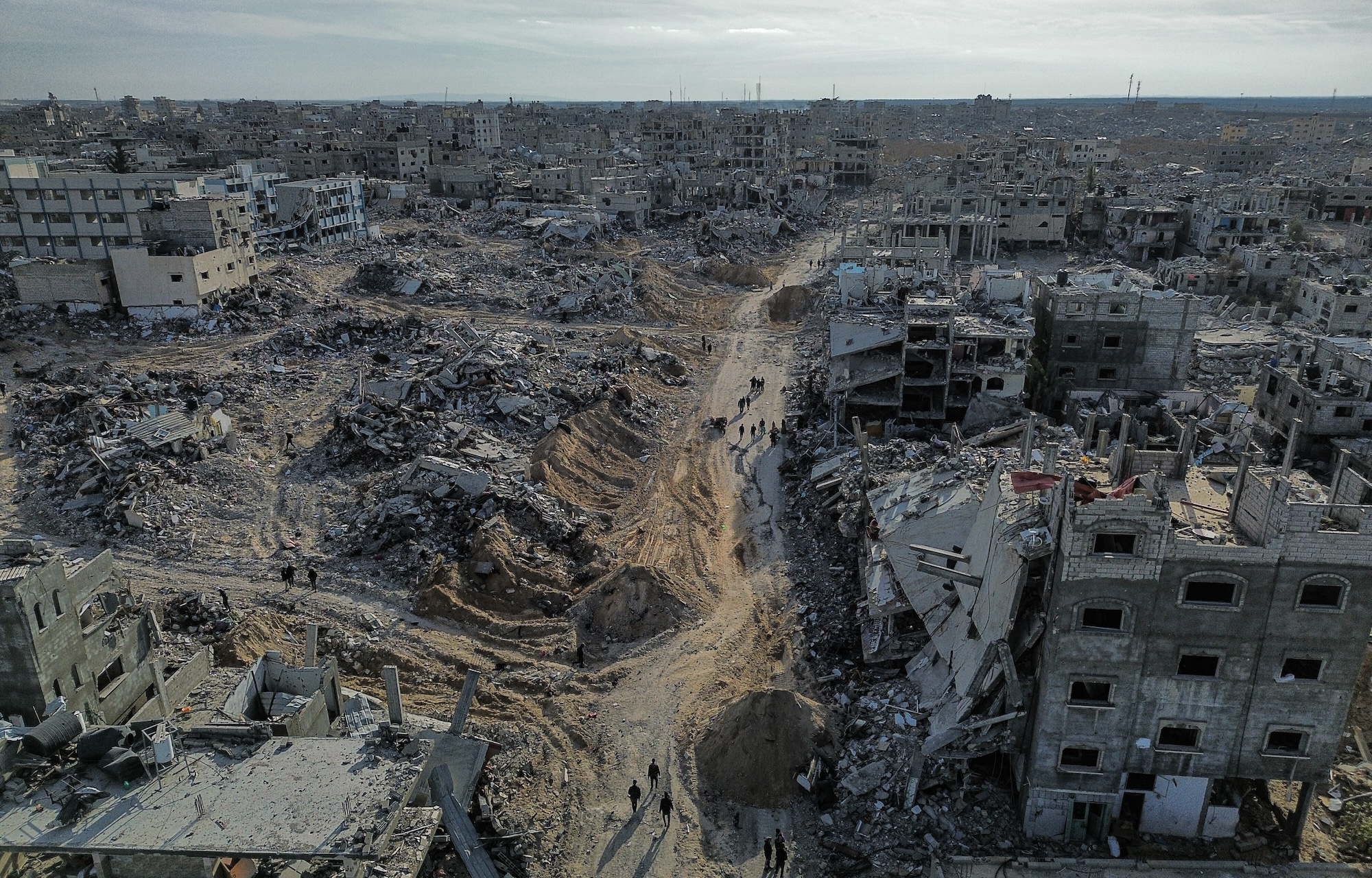 An aerial view of destroyed buildings with people walking among the rubble.