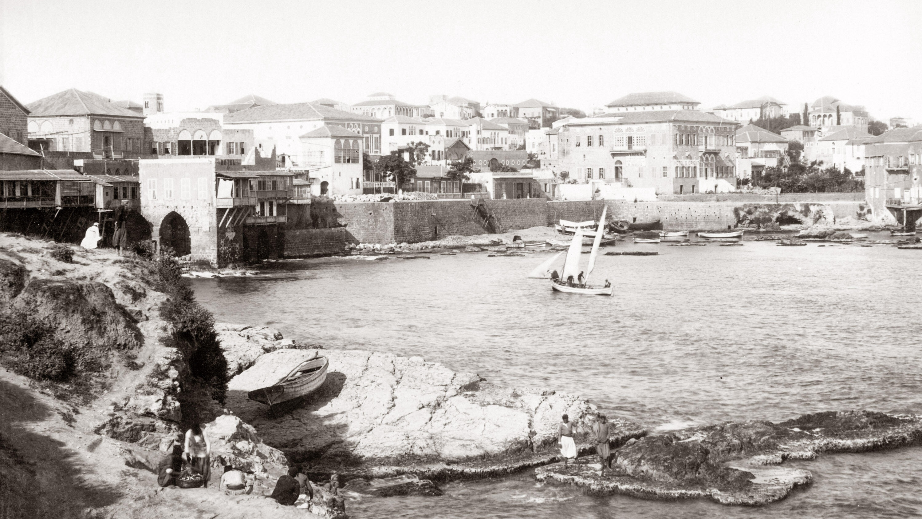 Black and white image of the Beirut seafront, with a sailing boat in the centre.