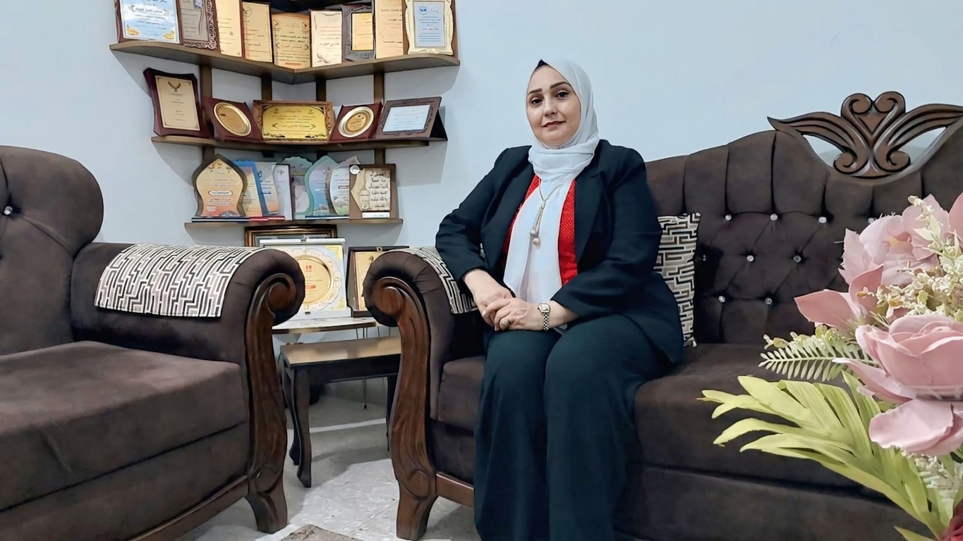 سيدة ترتدي الحجاب وتجلس على أريكة وخلفها رف من الدروع.