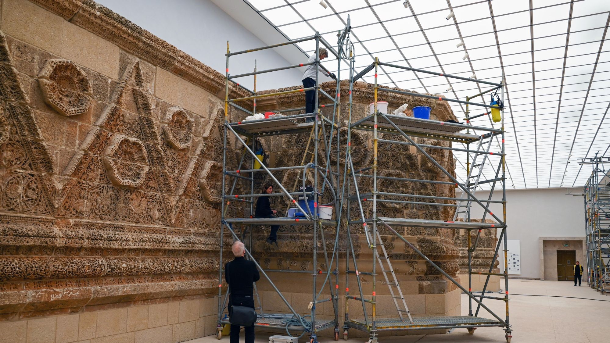 Eine Museumshallte mit archäologischer Fassade an der rechten Wand. Davor ein Baugerüst und Leute, die arbeiten.