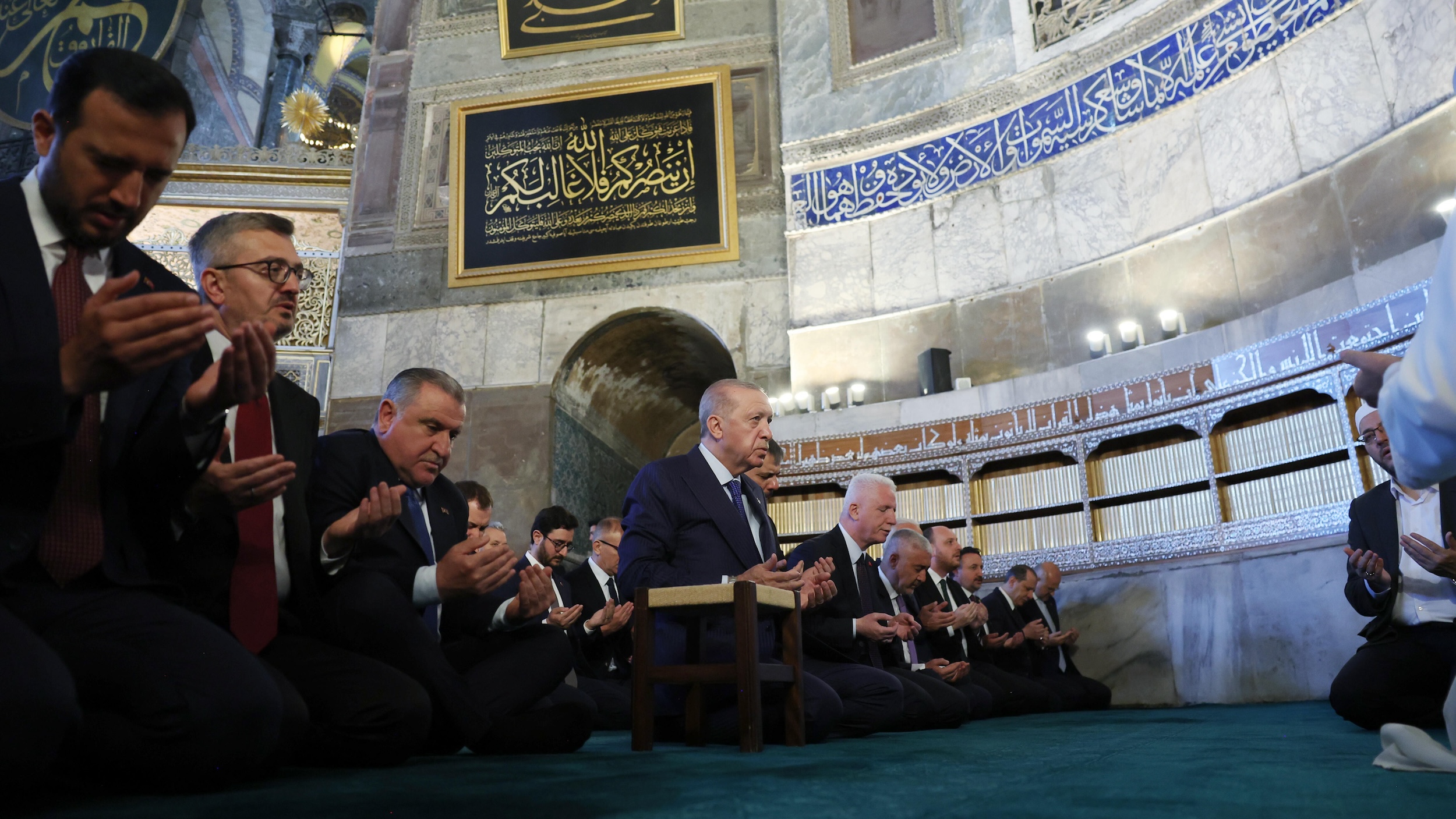 A row of men in suits pray in a mosque.
