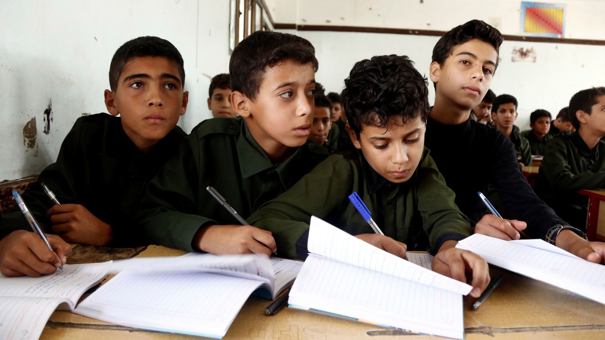 تلاميذ بزيهم المدرسي الزيتي يكتبون في كراريسهم خلال حصة دراسية.