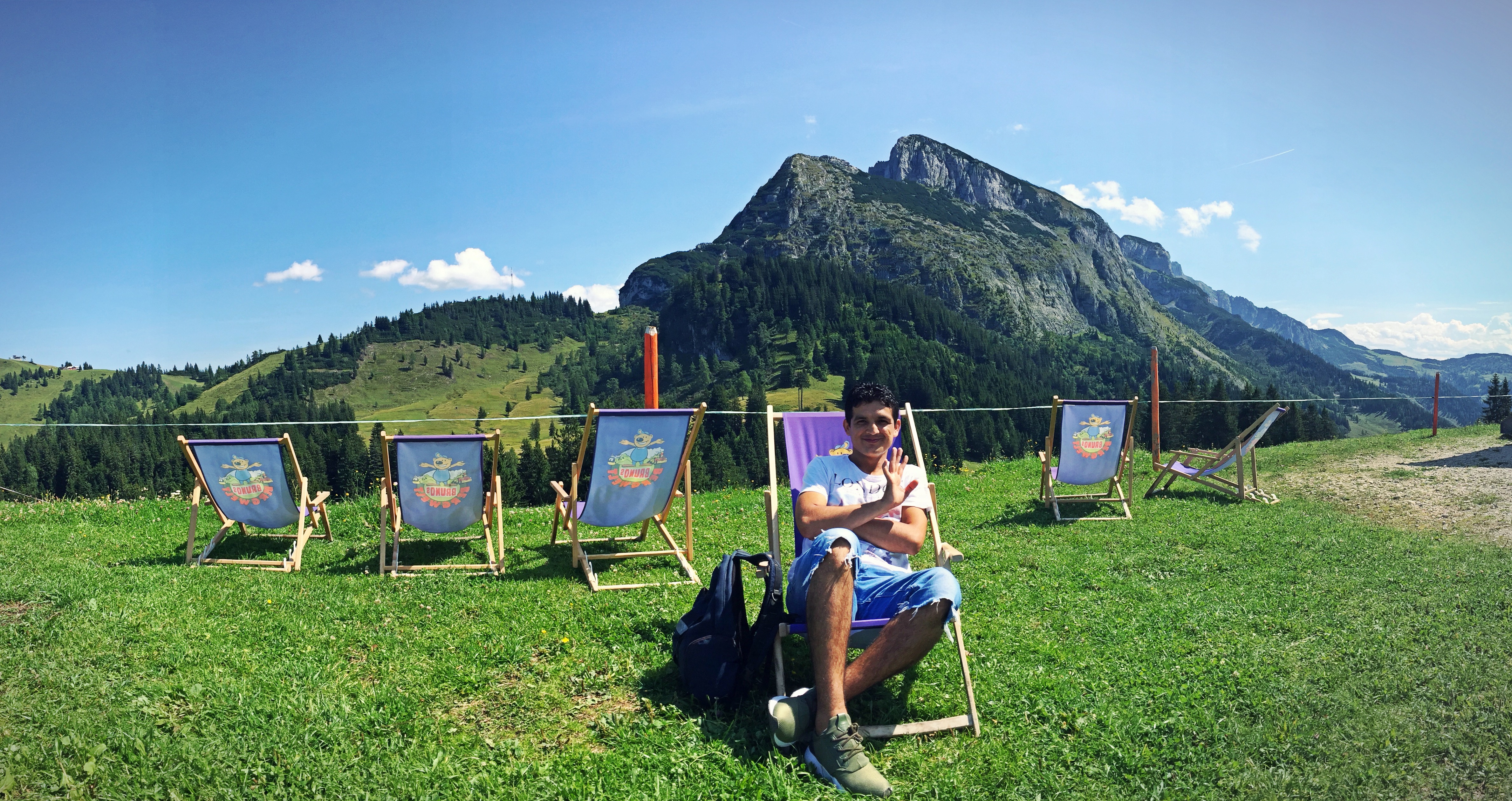 Ein Junge in Jeans sitzt in einem Sonnenstuhl vor einer Bergkulisse