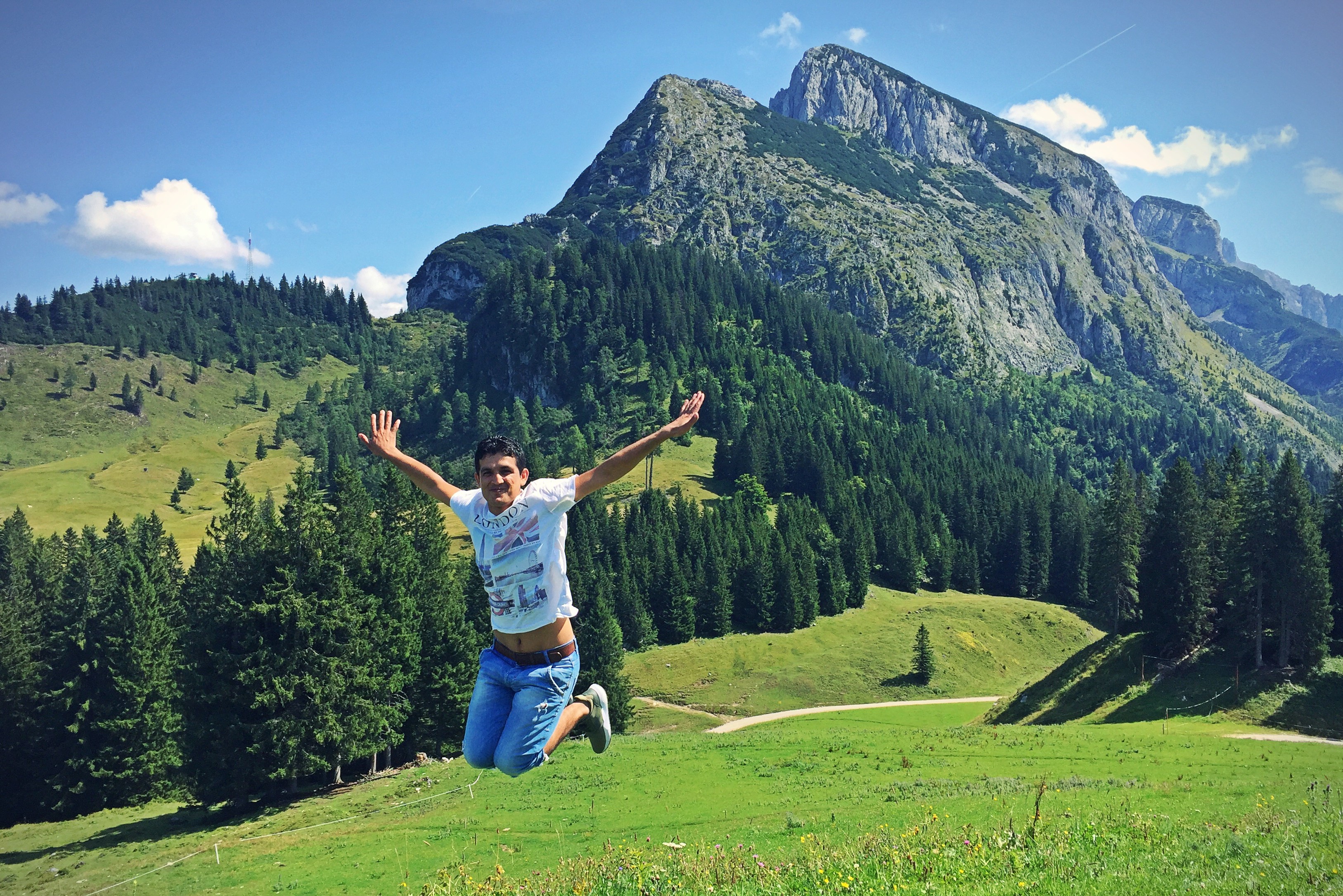 Ein Junge in Jeans springt vor einer Bergkulisse in die Luft.
