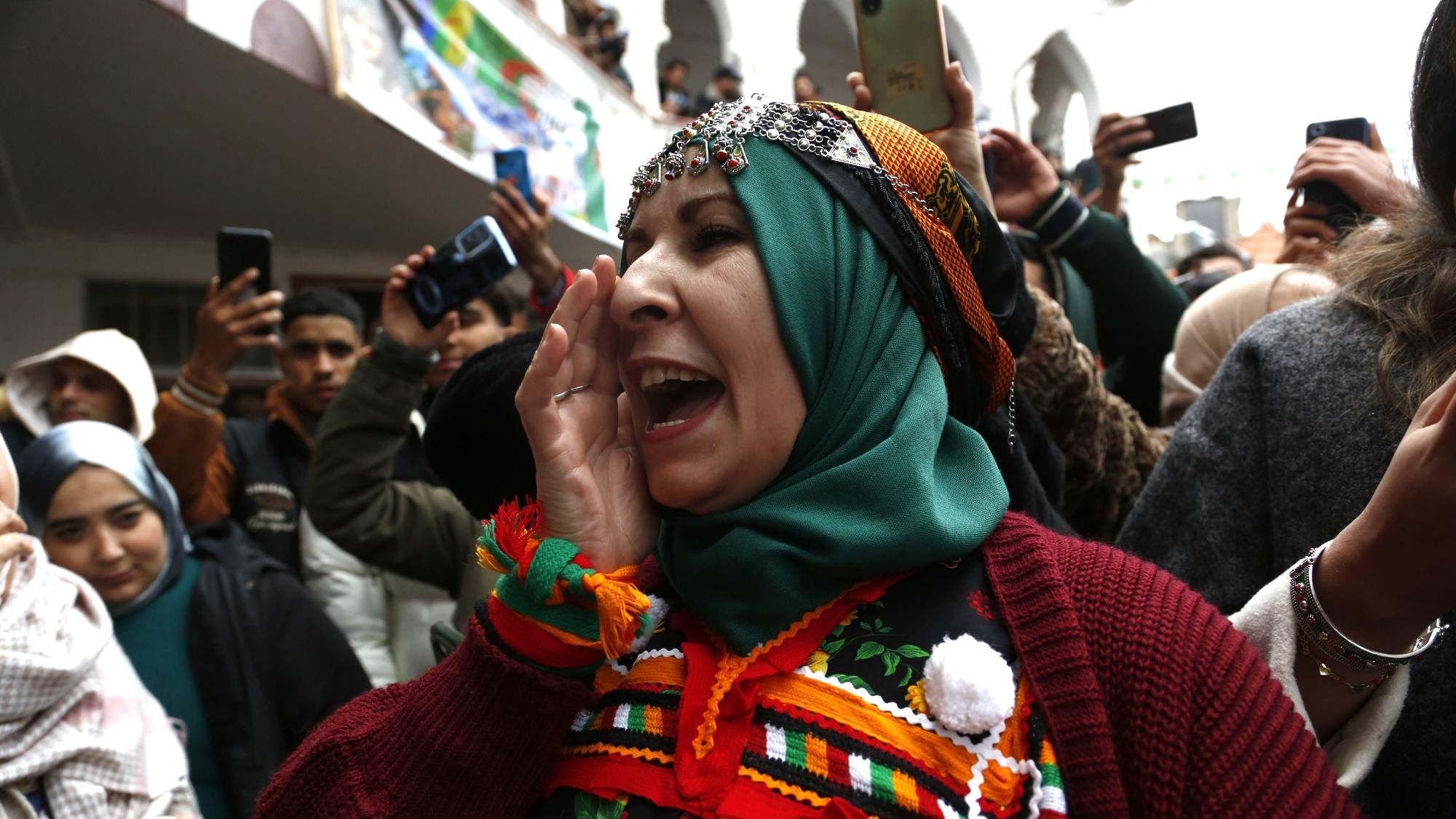 تظهر امرأة أمازيغية ترتدي زيًا تقليديًا وحُلياً تراثية، فيما يوثق الحاضرون المشهد بهواتفهم.