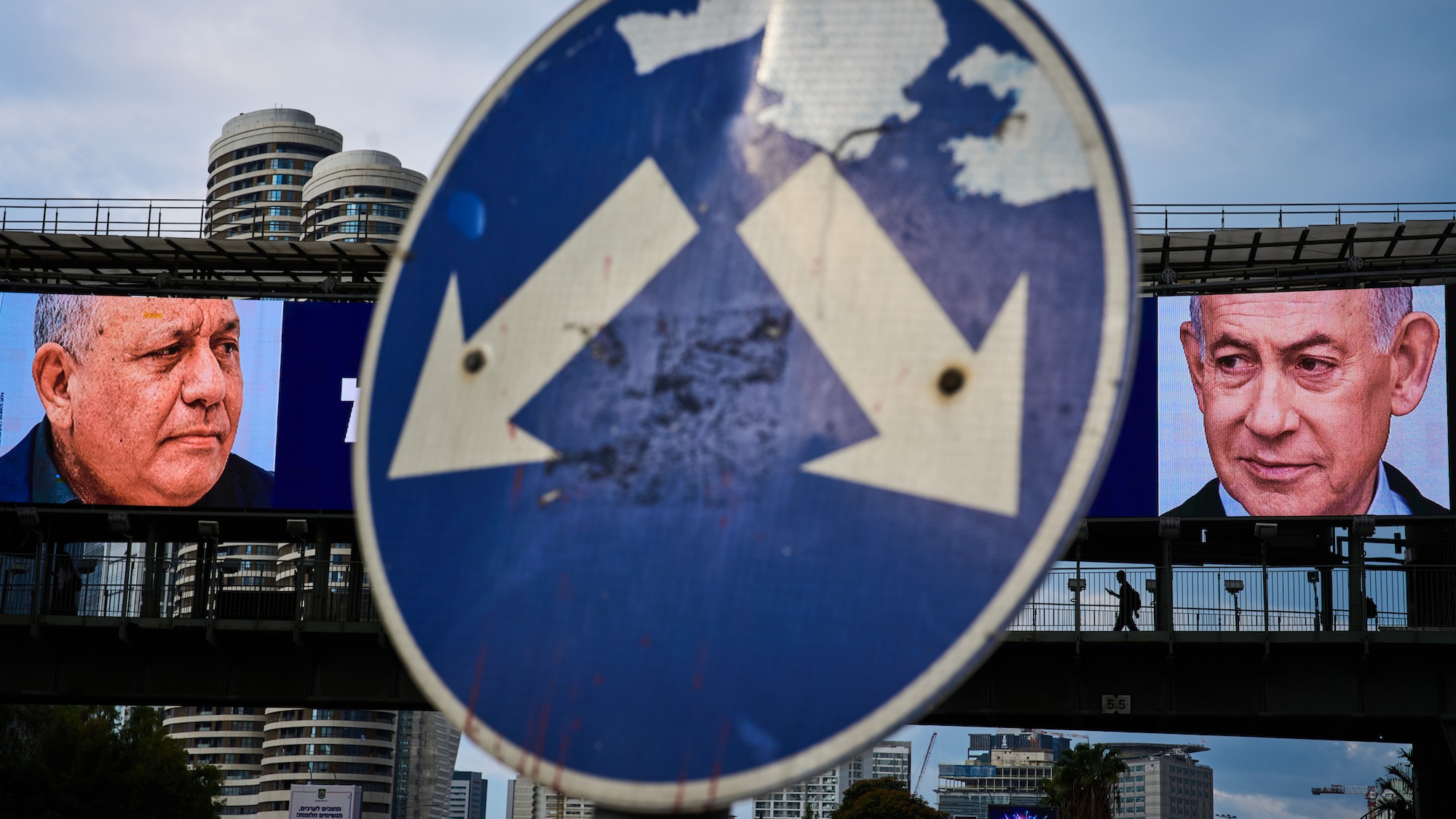 A road sign with two arrows pointing to the faces of Eisenkot and Netanyahu shown on large billboards in the background..
