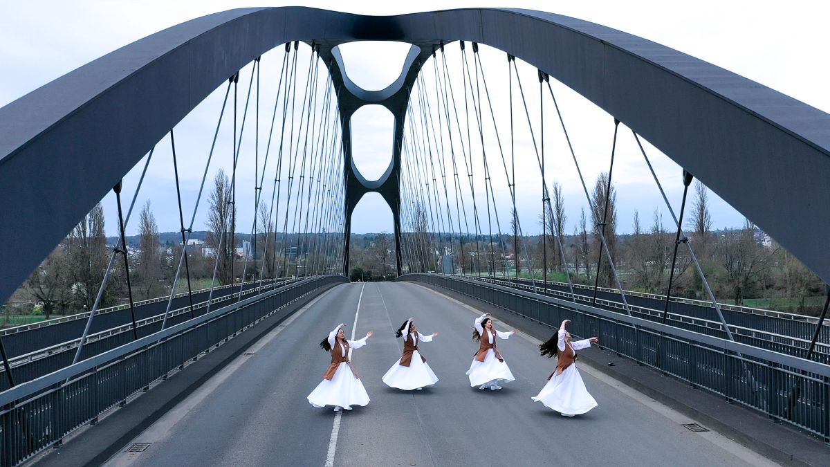 Auf einer bogenförmigen Autobahnbrücke tanzen vier Frauen in weißen Gewändern und langen dunklen Haaren.