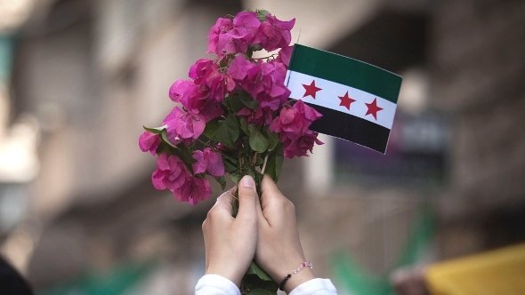 امرأة تحمل علَم الجيش السوري الحُرّ وباقة من الزهور. أ ب