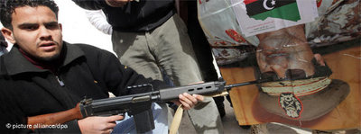 Libyan points a machine gun at a poster showing Gaddafi (photo: dpa)