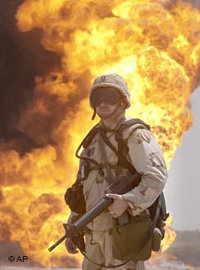 An unidentified US soldier stands guard as oil workers put out an oil well fire at Rumailah oil field, southern Iraq, April 2003 (photo: AP)