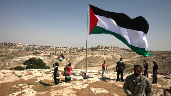 Palestinians hoist a huge Palestinian flag close to Israel's largest Jewish settlement of Maale Adumin on the outskirts of Jerusalem ahead of Obama's visit (photo: AFP/Getty Images)