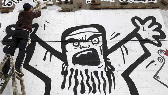 شاب يرسم على أحد الجدران في ميدان التحرير في القاهرة شكلاً يصوّر الإخوان المسلمين وكأنهم بعبع أو شبح مرعب. رويترز   