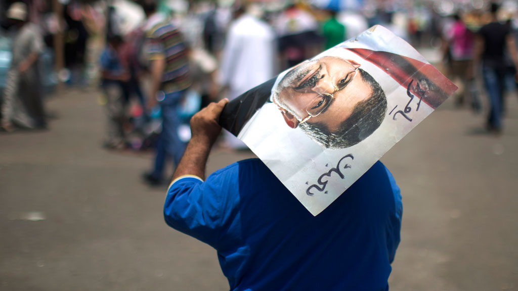 An Egyptian supporter of the Muslim Brotherhood walks holding a poster featuring deposed president Mohamed Morsi during a rally to support him on July 6, 2013 outside Cairo's Rabaa al-Adawiya mosque (photo: credit should read Mahmud Hams/AFP/Getty Images)