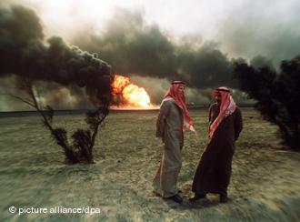 Two Kuwaiti men standing in the desert, in the background burning oil fields, set on fire by Iraqi troops (photo: picture-alliance/dpa)