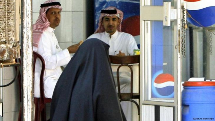 امرأة منقبة في مدينة جدة السعودية تمر بجوار مقهى يجلس فيه بعض الرجال.   Foto: picture-alliance/dpa