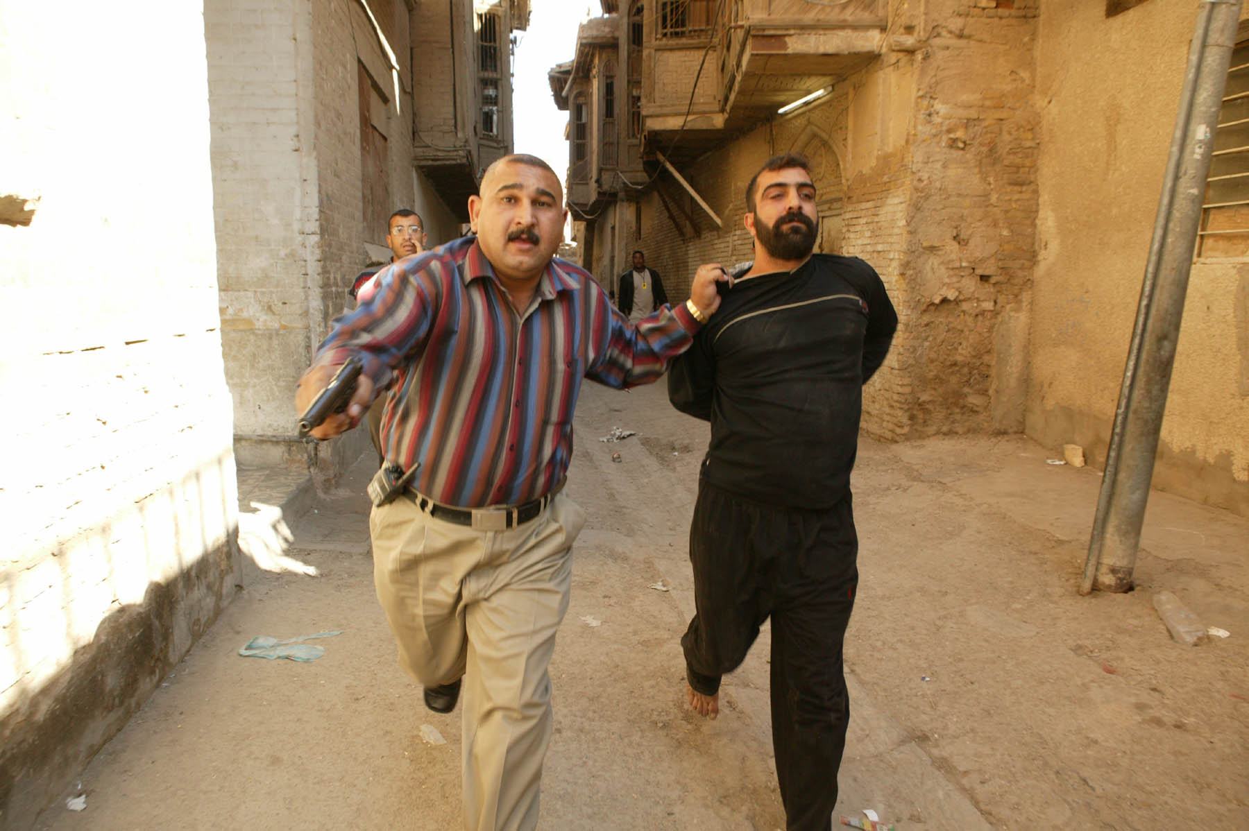 A member of the Iraqi Major Crimes Unit runs along a street with an arrested criminal (photo: Michael Kamber)
