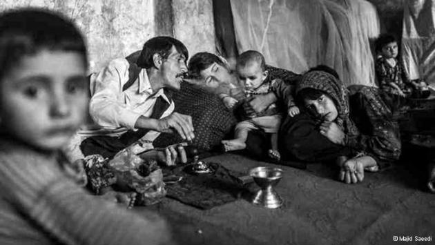 A man smokes opium in the presence of women and children, exhaling smoke into an infant's face (photo: Majid Saeedi)