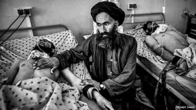 A man touches the chest and arm of another man lying injured in a hospital bed (photo: Majid Saeedi)