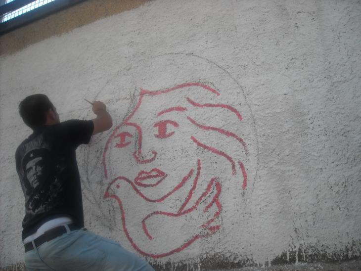 A man paints the logo of the Palestinian Working Woman Society for Development (PWWSD) on a wall (photo: PWWSD)