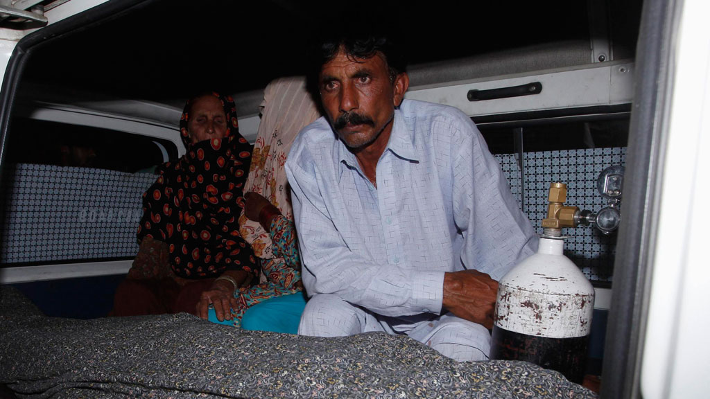 Mohammad Iqbal sits next to his wife Farzana's body in an ambulance outside a morgue in Lahore, Pakistan, 27 May 2014 (photo: Reuters)