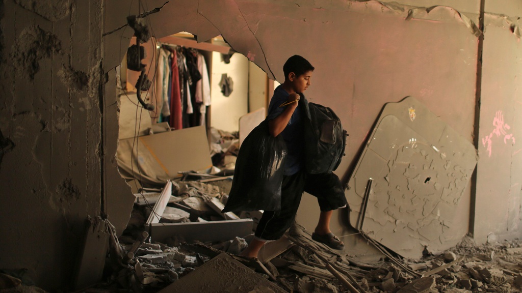 A Palestinian boy carries his belongings inside his family's ruined house in Gaza City, July 16, 2014. REUTERS/Mohammed Salem 