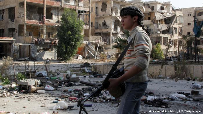 A young combatant stands in front of a row of bombed-out buildings in Syria (photo: AFP/Getty Images)
