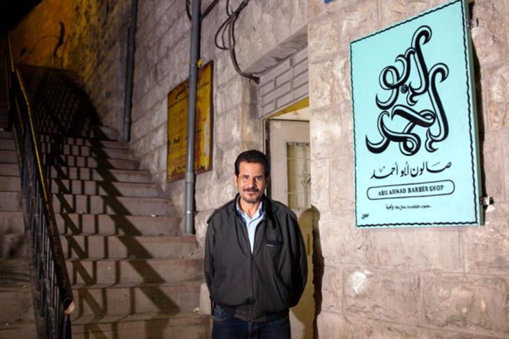 Abu Ahmad in front of his barber shop with its brand new sign (photo: Essa Almasri/Wajha)
